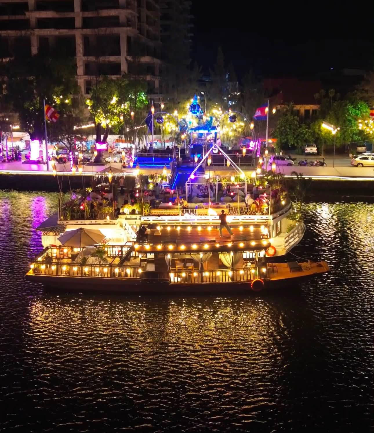 Night aerial of the Kdam Kampot boat outlined in warm lights on the dark Kampot river