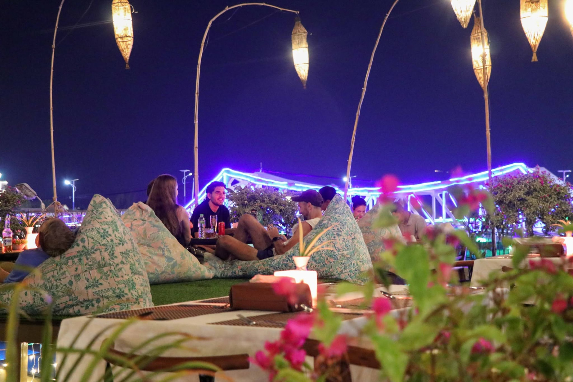 Friends relaxing on bean bags on the deck with the blue-lit Old Bridge behind