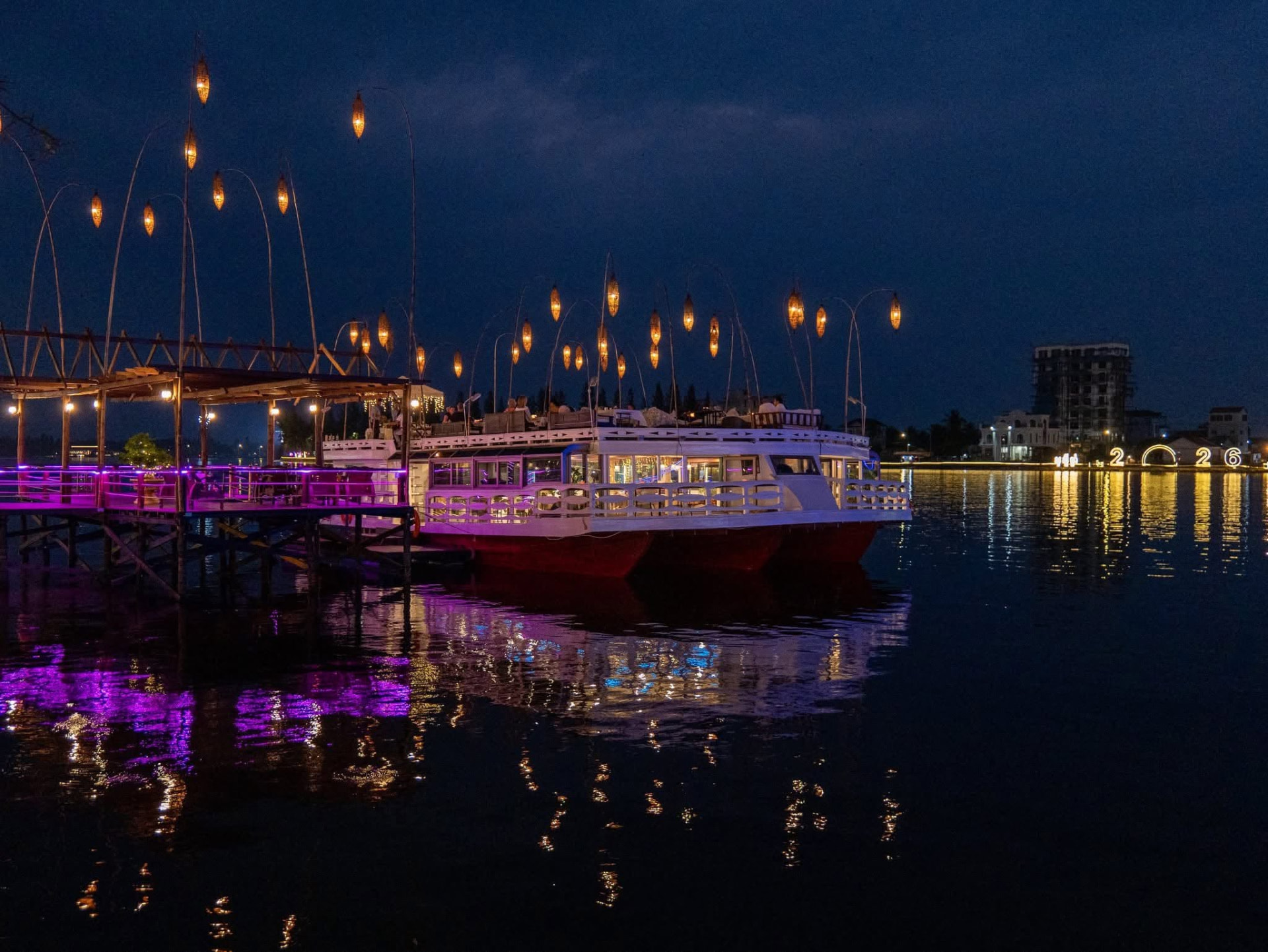 The Kdam Kampot boat moored beside the lantern-lit jetty at night