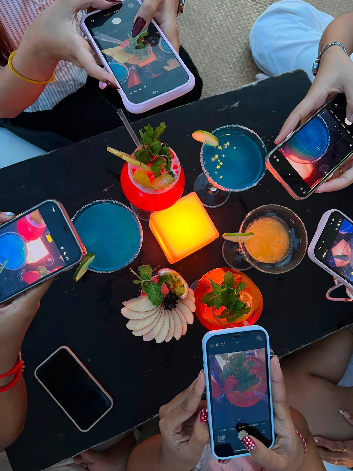Overhead view of guests photographing colourful cocktails around a candlelit table