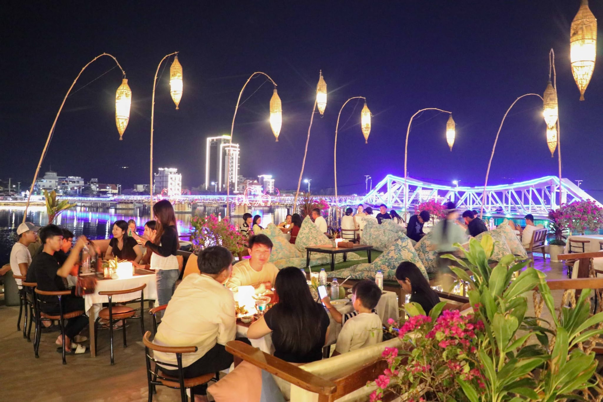 A full deck of guests under bamboo lanterns with the blue-lit Old Bridge across the water