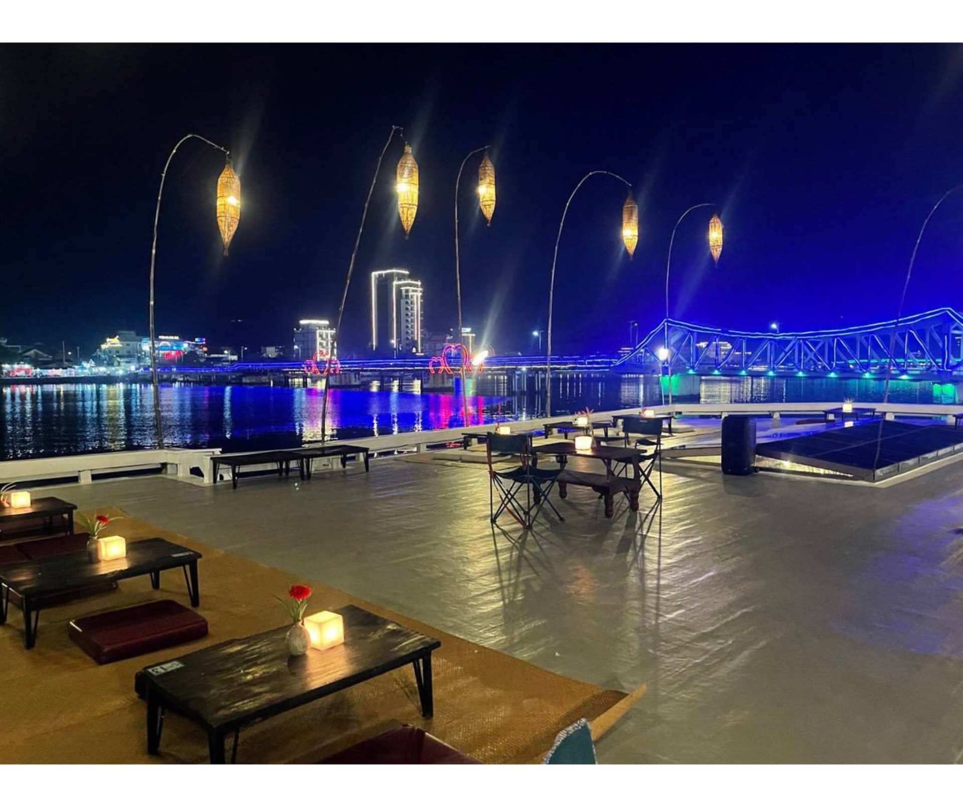 Low tables and candles on the Kdam Kampot deck facing the blue-lit Old Bridge