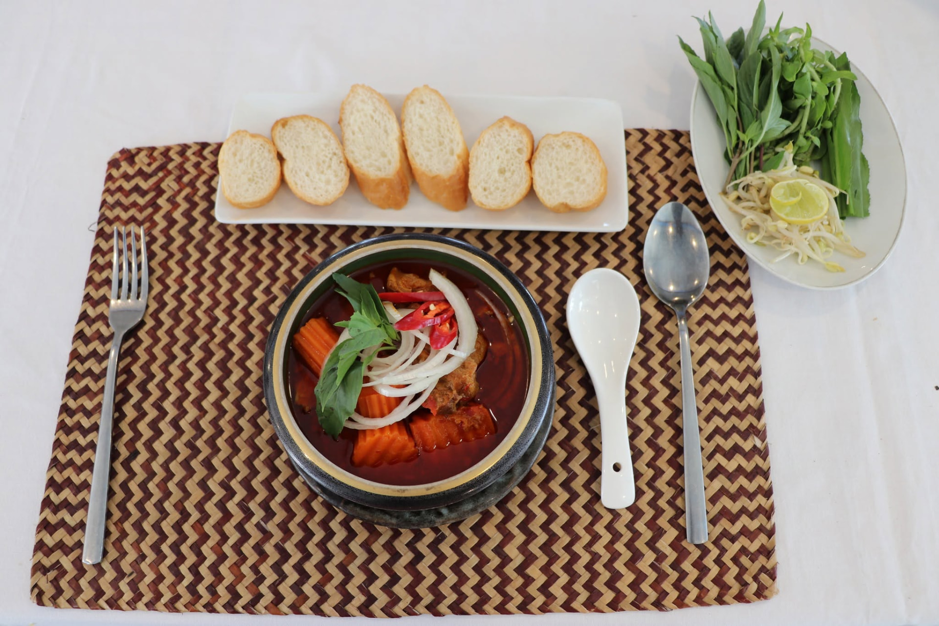 Khmer curry served in a clay pot with fresh herbs, bean sprouts and warm baguette