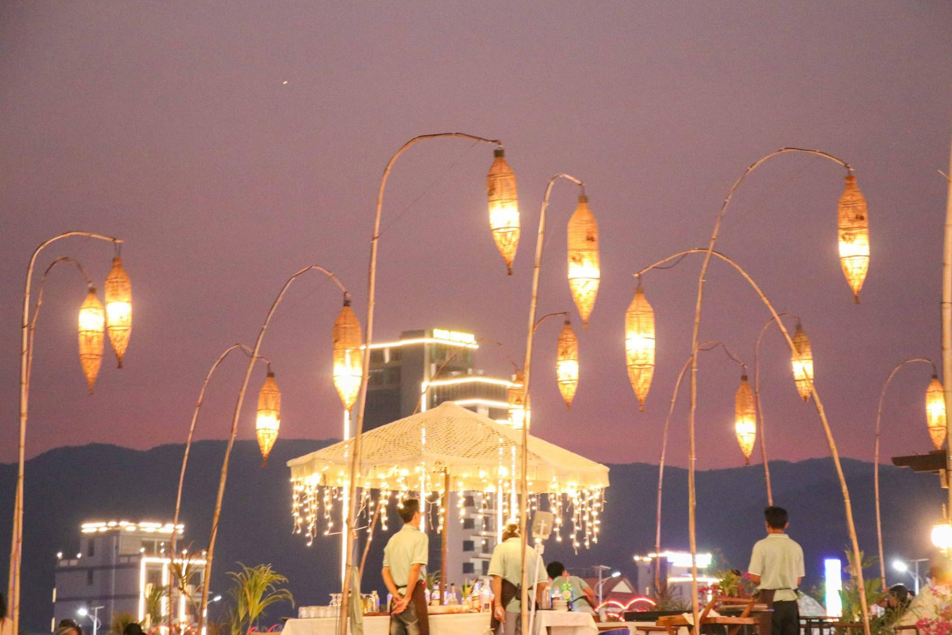 Bamboo lanterns arching over the deck against a pink Kampot sunset